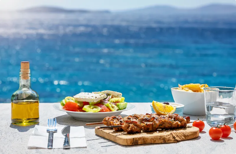 En grekisk måltid serverad utomhus med havet i bakgrunden.